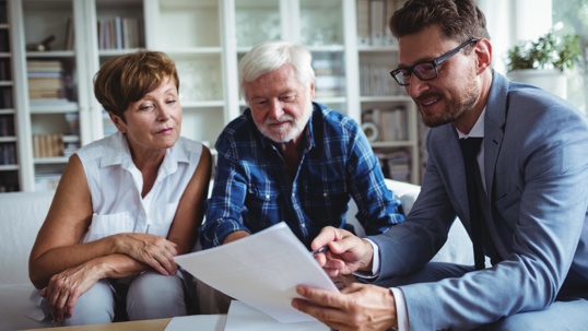 Three people sitting together on a couch looking at paperwork.
